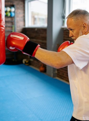 Senior man in a white shirt boxing with a heavy bag indoors for fitness.